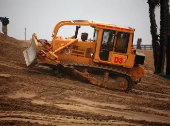 A crawler dozer with its blade lowered working reddish earth beside palms — dozer insurance in Connecticut
