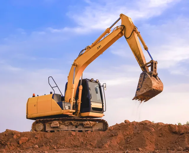 A tracked excavator with its arm raised on a mound of red earth against a blue sky — excavator insurance in Nevada