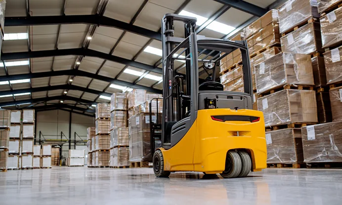 A forklift standing in a warehouse aisle between tall racks of palletised stock — forklift insurance in Oklahoma