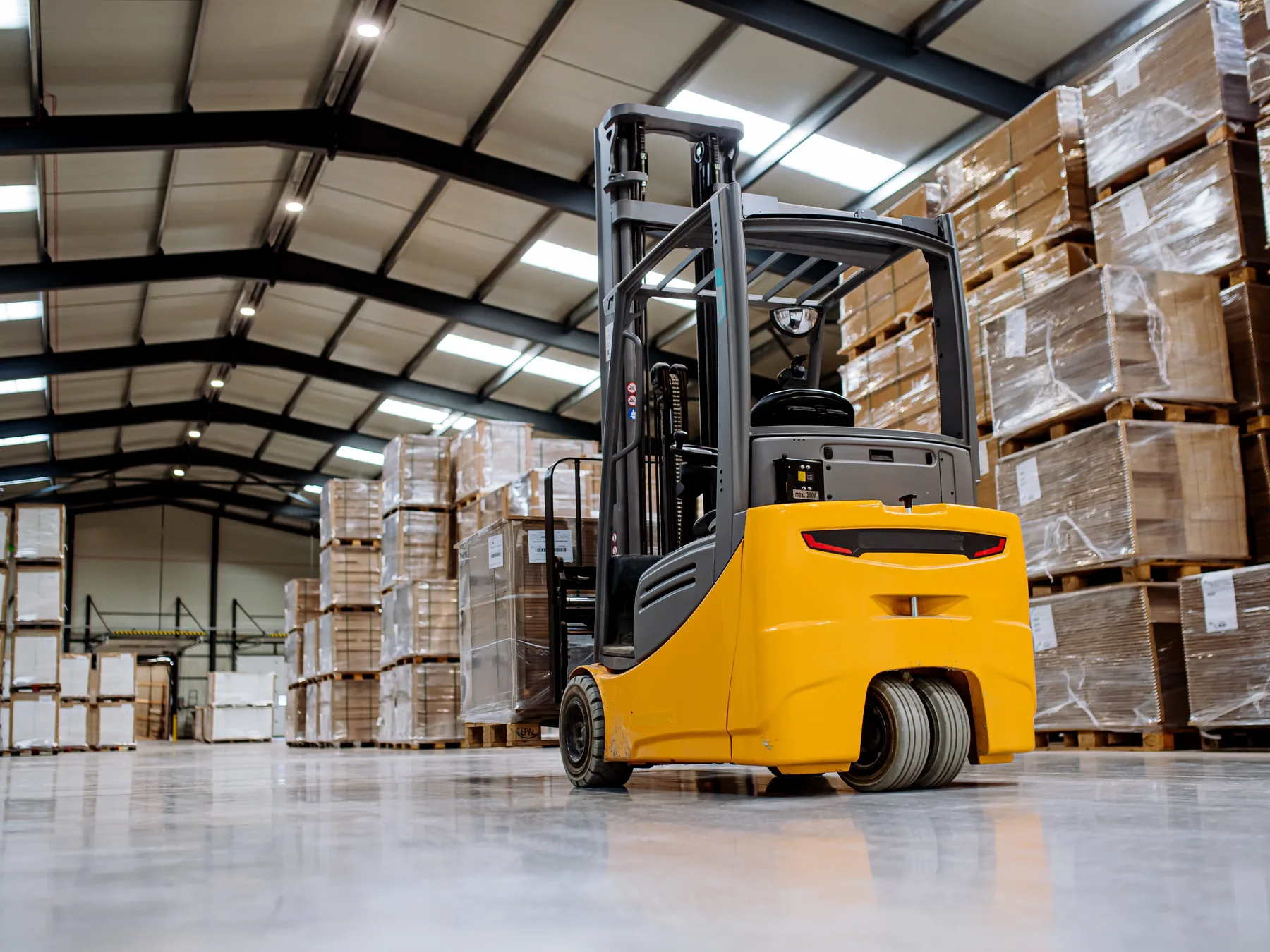 A forklift standing in a warehouse aisle between tall racks of palletised stock — forklift insurance in Indiana