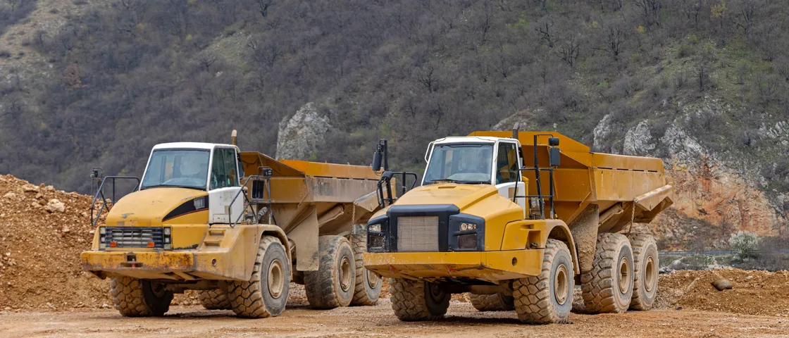 Articulated dump haulers parked on a dirt quarry floor below a rocky hillside
