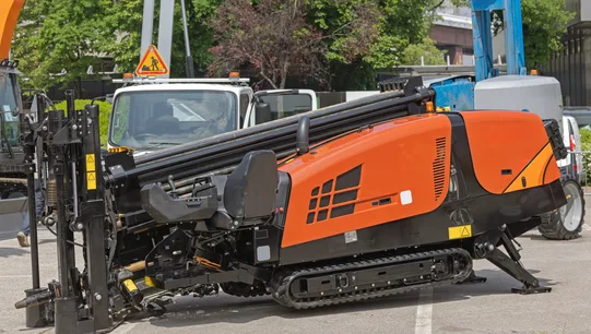 A tracked horizontal directional drilling rig set up on paved ground beside trees