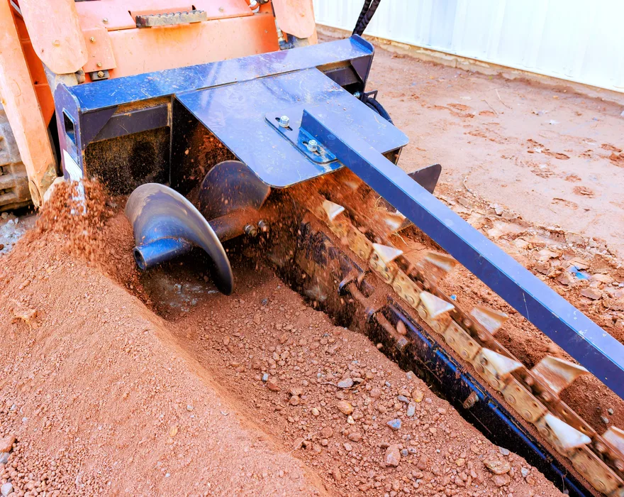 A trencher digging wheel cutting an open trench through red soil