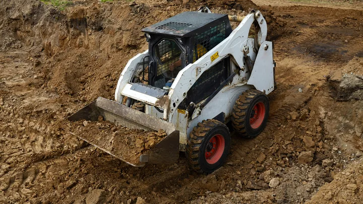 A skid steer loader with a raised bucket working a mound of dark earth — heavy equipment insurance in Ohio