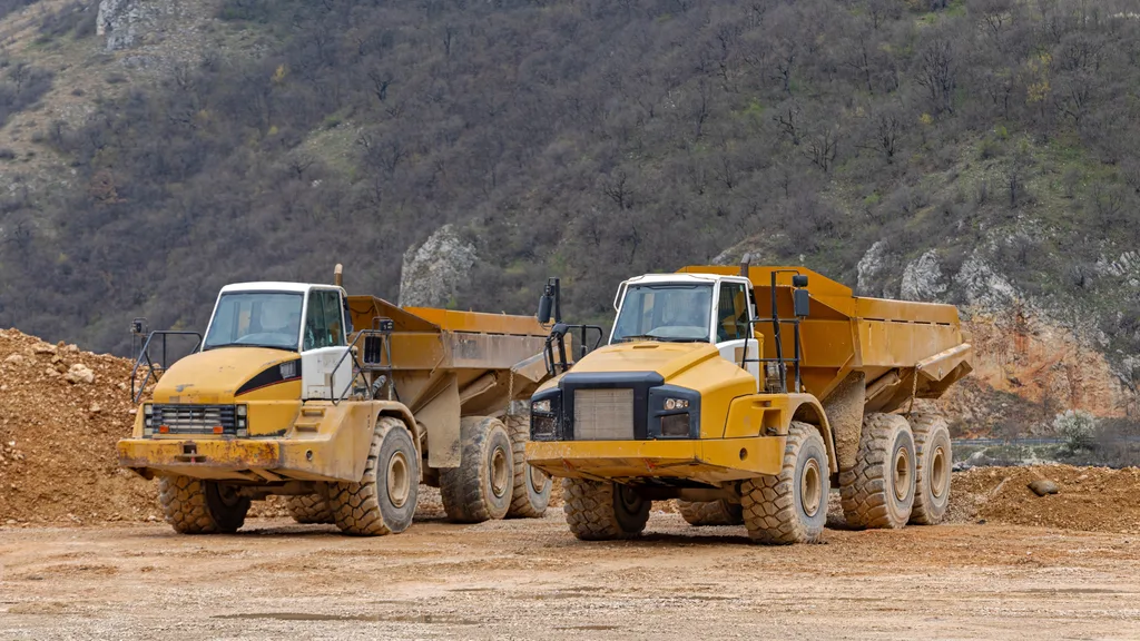 Articulated dump haulers parked on a dirt quarry floor below a rocky hillside — heavy equipment insurance in Indiana
