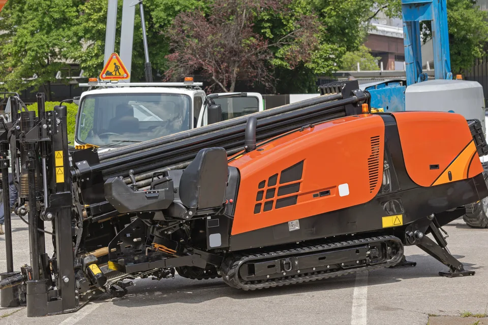 A tracked horizontal directional drilling rig set up on paved ground beside trees