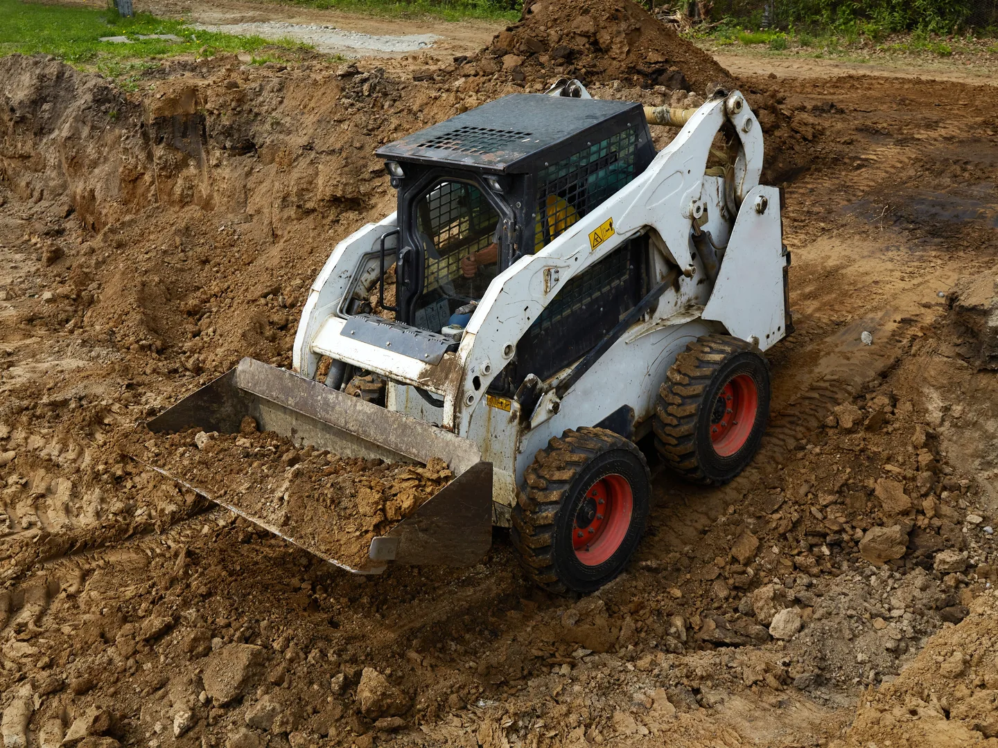 A skid steer loader with a raised bucket working a mound of dark earth — skid steer insurance in Illinois
