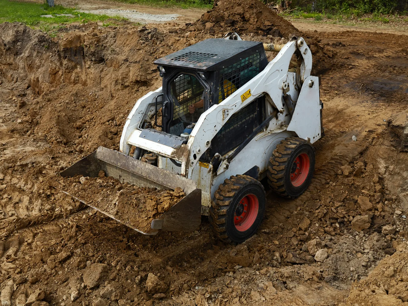 A skid steer loader with a raised bucket working a mound of dark earth — skid steer insurance in Texas
